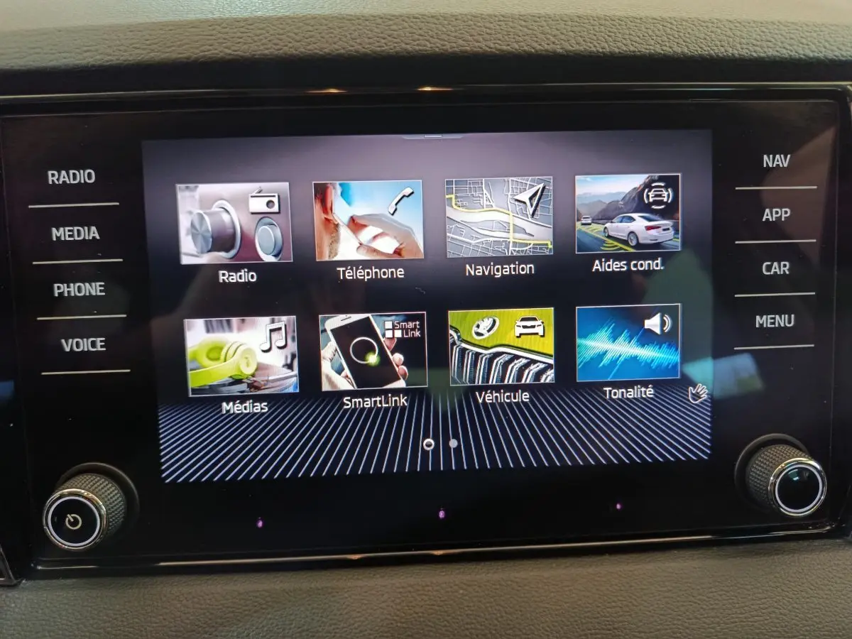 Écran tactile central du Skoda Karoq blanc 2024 affichant les menus radio, téléphone, navigation et aides à la conduite.