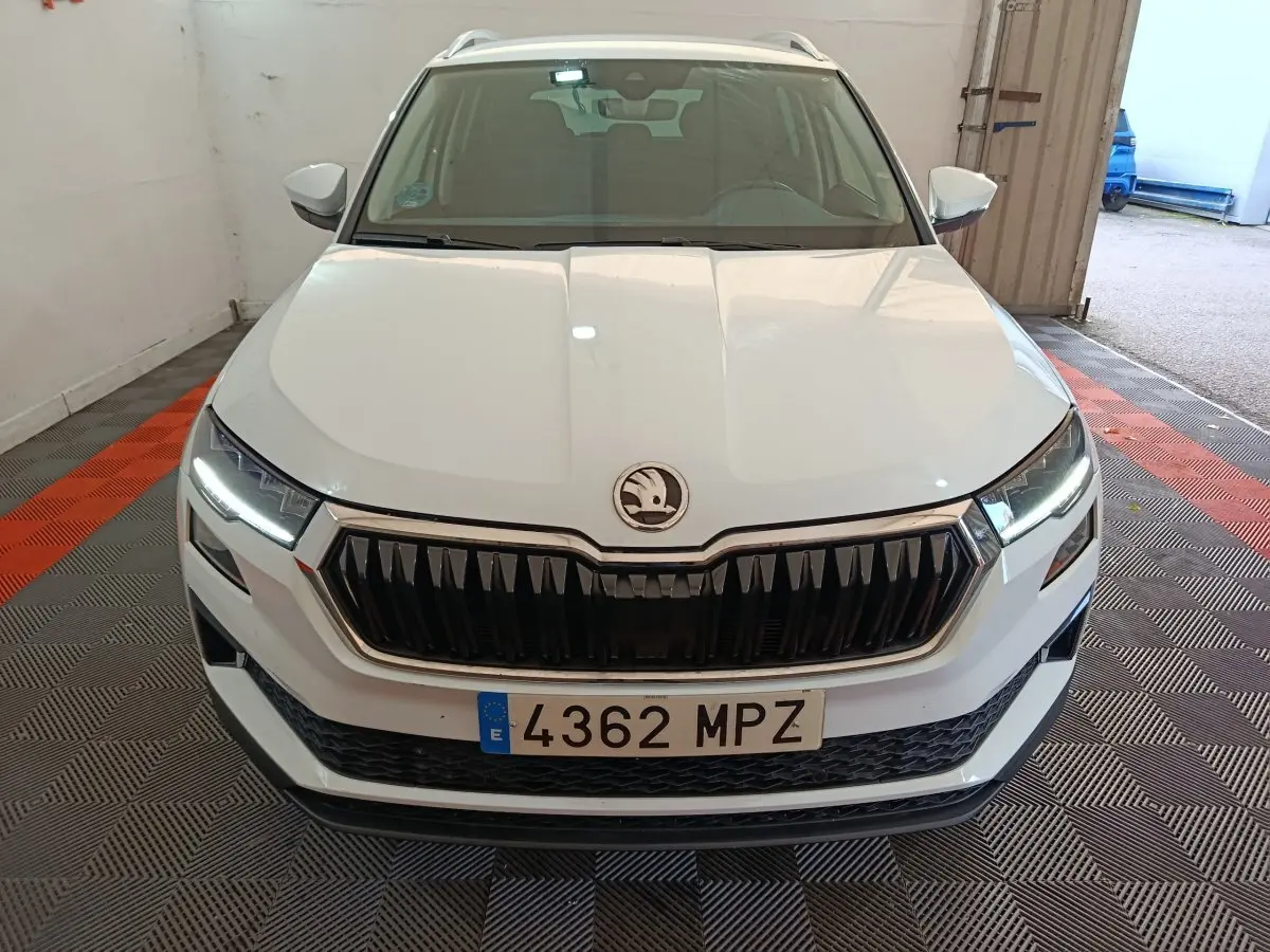 Vue frontale d'un Skoda Karoq blanc 2024 avec calandre noire et phares LED allumés dans un garage.