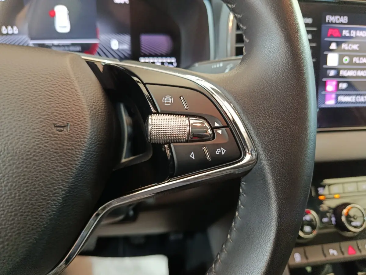 Gros plan sur les commandes multifonctions du volant cuir du Skoda Karoq blanc, avec écran tactile en arrière-plan.
