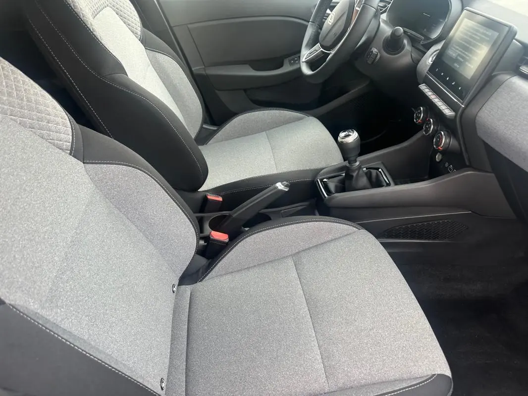 Vue intérieure côté conducteur de la Renault Clio V dCi 100 Evolution 2025, sièges gris et levier de vitesse manuel.