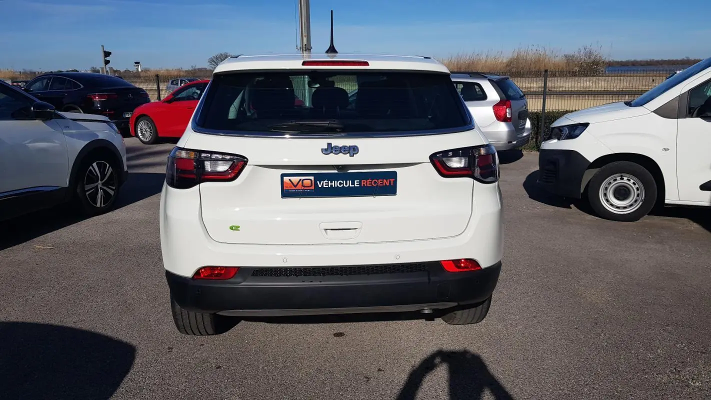 Vue arrière d'un Jeep Compass blanc 2024 avec feux LED et logo Jeep visible sur un parking extérieur.