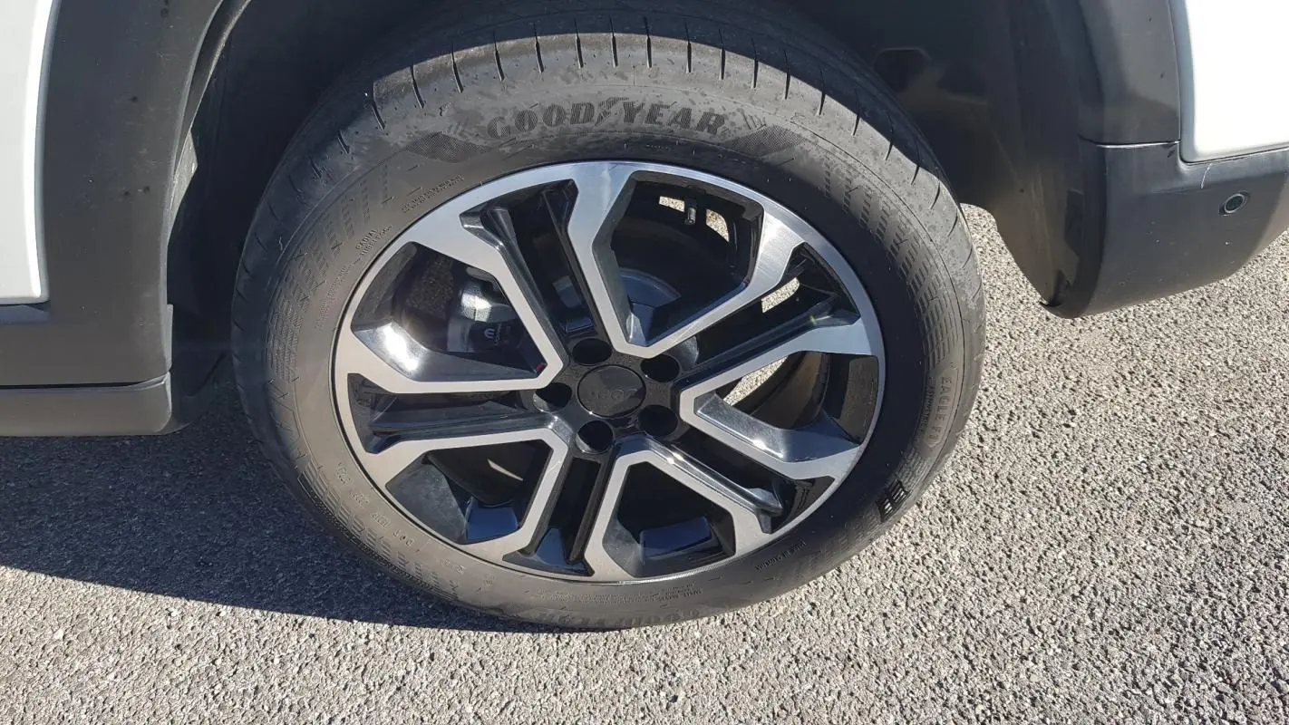 Gros plan sur la jante alliage 18 pouces noire et argent du côté avant droit d'un Jeep Compass blanc.