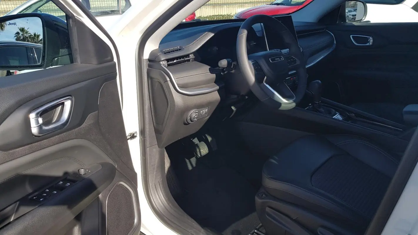 Intérieur côté conducteur du Jeep Compass blanc 2024, avec tableau de bord et volant visibles, porte ouverte.
