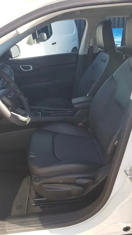 Vue intérieure côté conducteur du Jeep Compass blanc 2024, sièges noirs avec accoudoir central et commandes visibles.