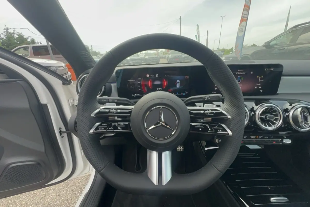 Vue intérieure centrée sur le volant cuir multifonctions noir de la Mercedes Classe A 200D BVA Exclusive Design blanche.