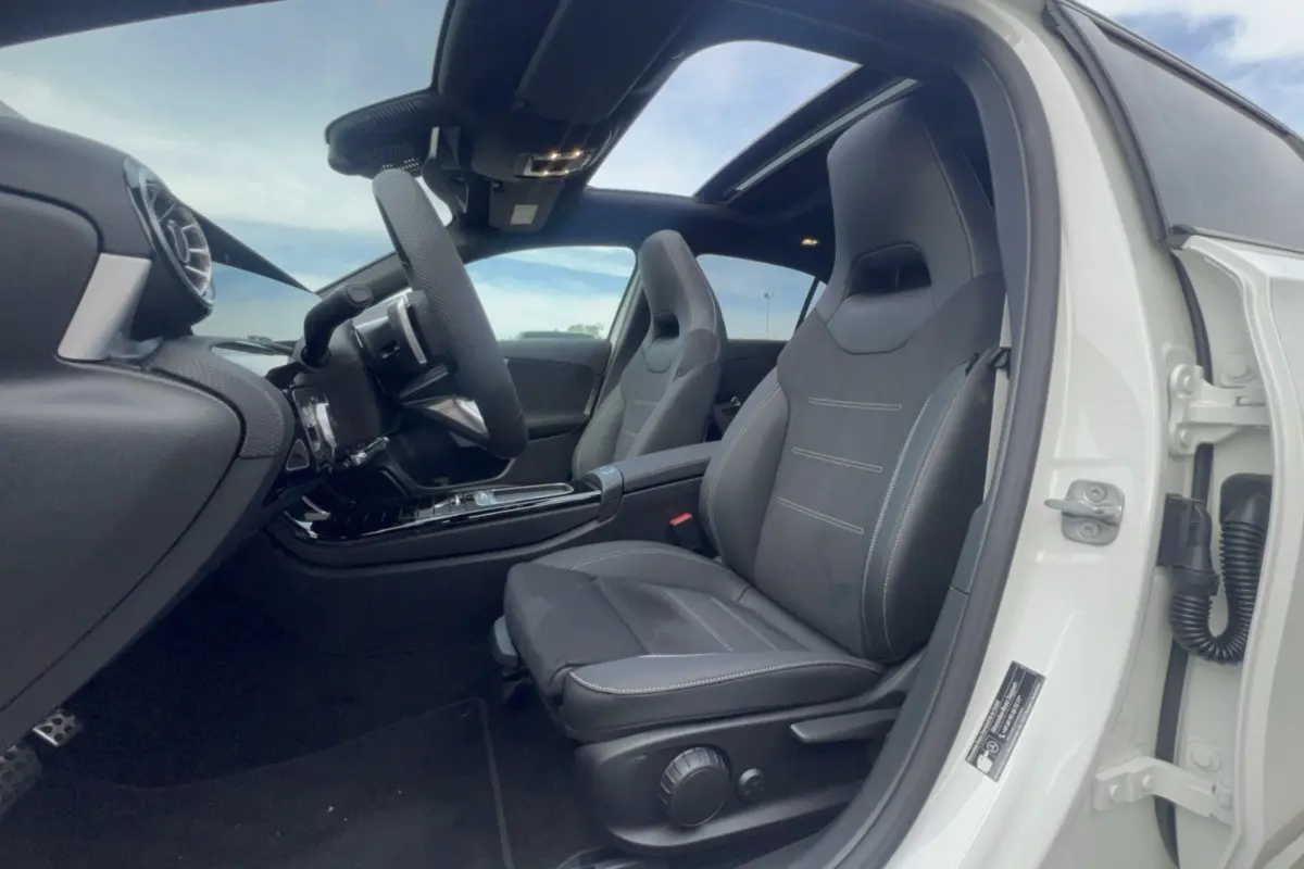 Vue intérieure côté conducteur d'une Mercedes Classe A 200D Exclusive Design blanche avec sièges sport noirs et toit ouvrant panoramique.