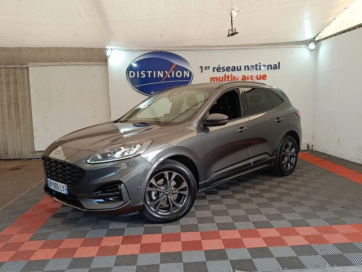 Ford Kuga gris foncé en 3/4 avant droit, avec jantes noires et calandre imposante dans un showroom.