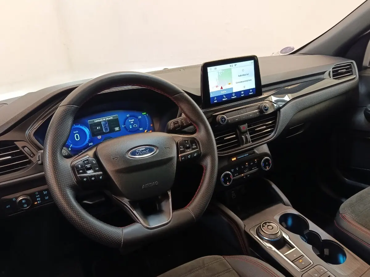 Vue intérieure du tableau de bord et volant cuir noir avec surpiqûres rouges du Ford Kuga gris foncé 2023.