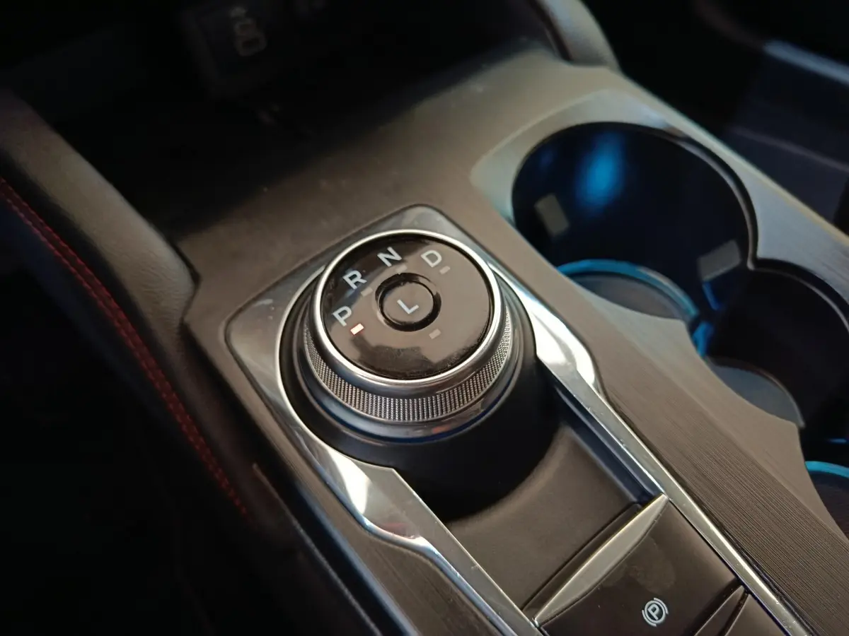 Gros plan sur la molette de boîte automatique noire et argentée du Ford Kuga gris foncé, avec porte-gobelets à côté.