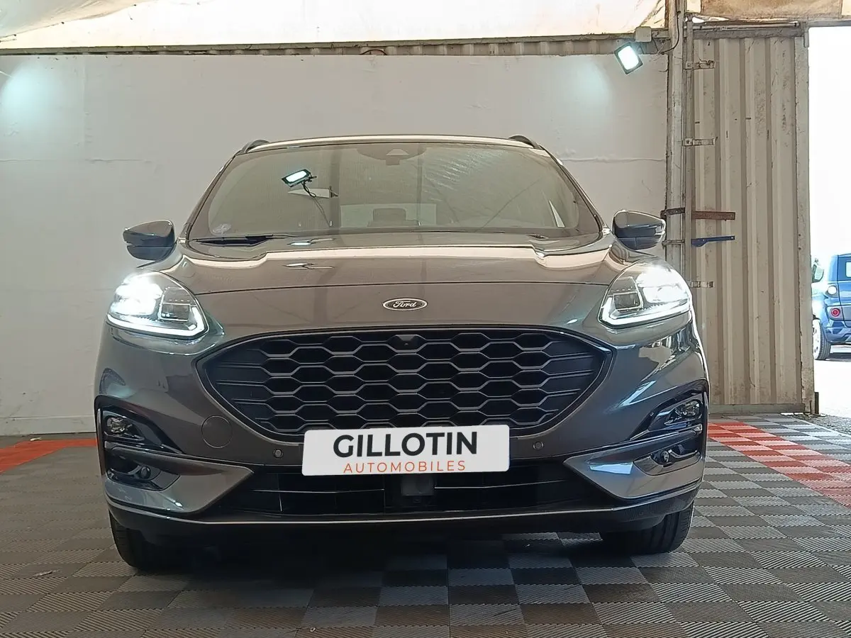 Vue frontale d'un Ford Kuga gris foncé 2023 avec phares LED allumés et calandre noire hexagonale.