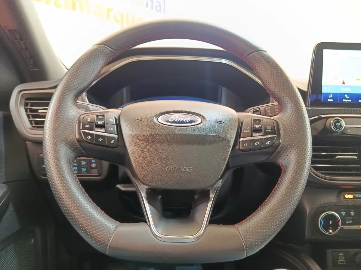 Vue rapprochée du volant cuir noir avec surpiqûres rouges du Ford Kuga gris foncé, tableau de bord et écran tactile visibles.