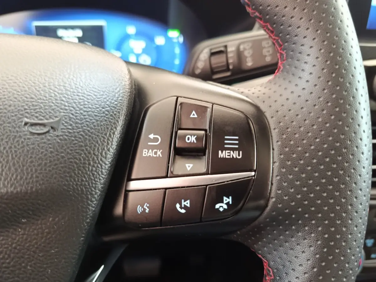 Gros plan sur les commandes multifonctions à gauche du volant en cuir perforé du Ford Kuga gris foncé 2023.