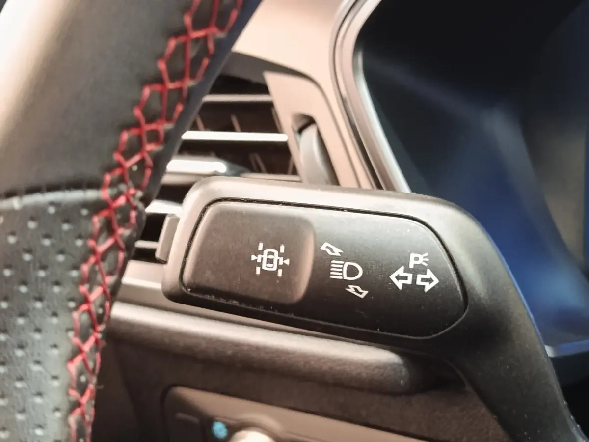 Détail du commodo de phares et clignotants sur le volant avec surpiqûres rouges, intérieur Ford Kuga gris foncé.