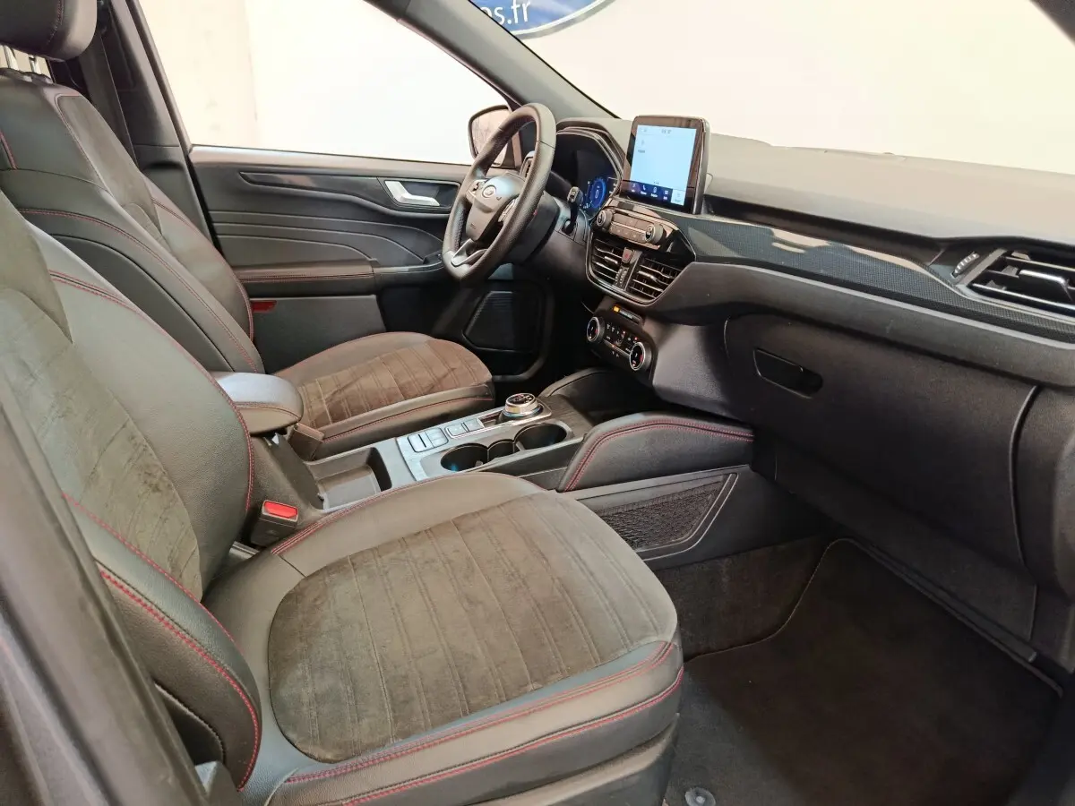 Intérieur avant du Ford Kuga 2023, vue côté gauche, sièges gris avec surpiqûres rouges et écran tactile central.