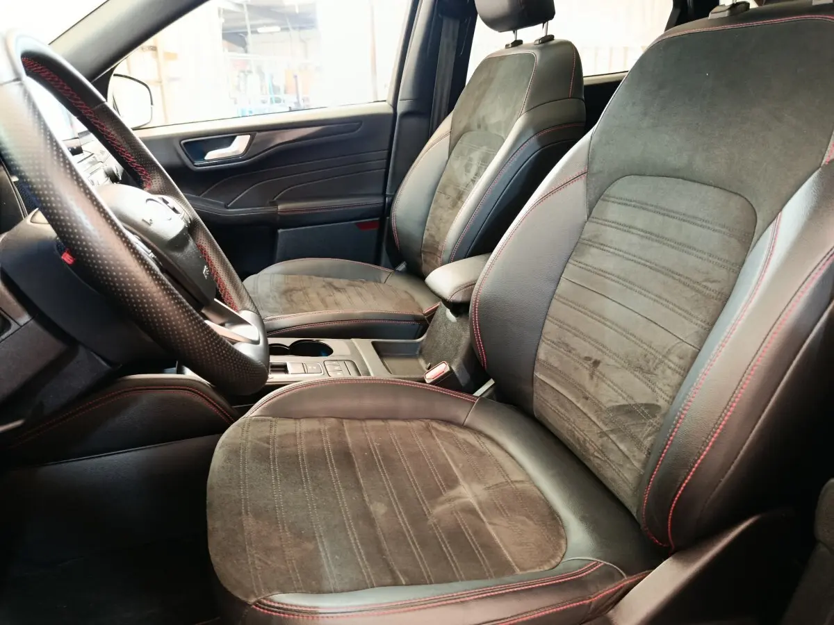 Vue intérieure côté conducteur du Ford Kuga 2023, sièges en cuir et alcantara gris foncé avec surpiqûres rouges.