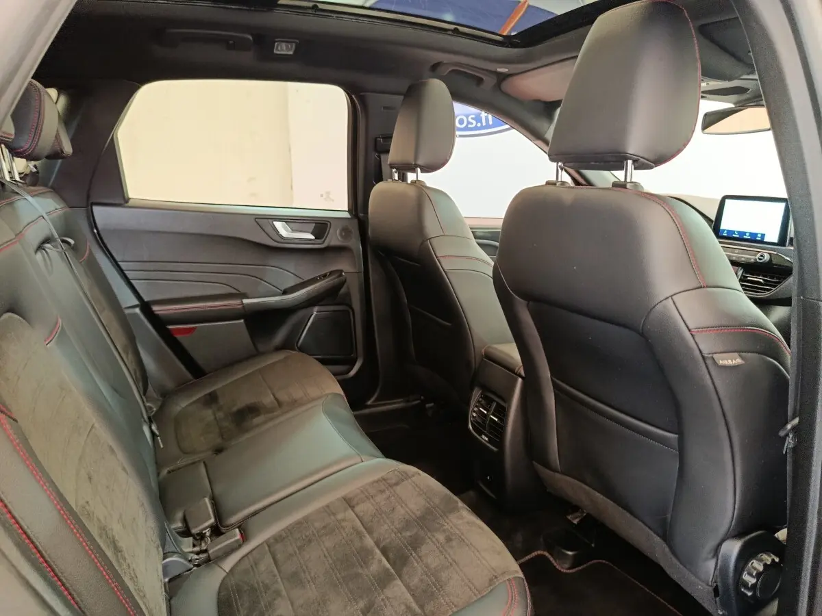 Vue intérieure arrière droite du Ford Kuga 2023, sièges noirs avec surpiqûres rouges et toit ouvrant panoramique.