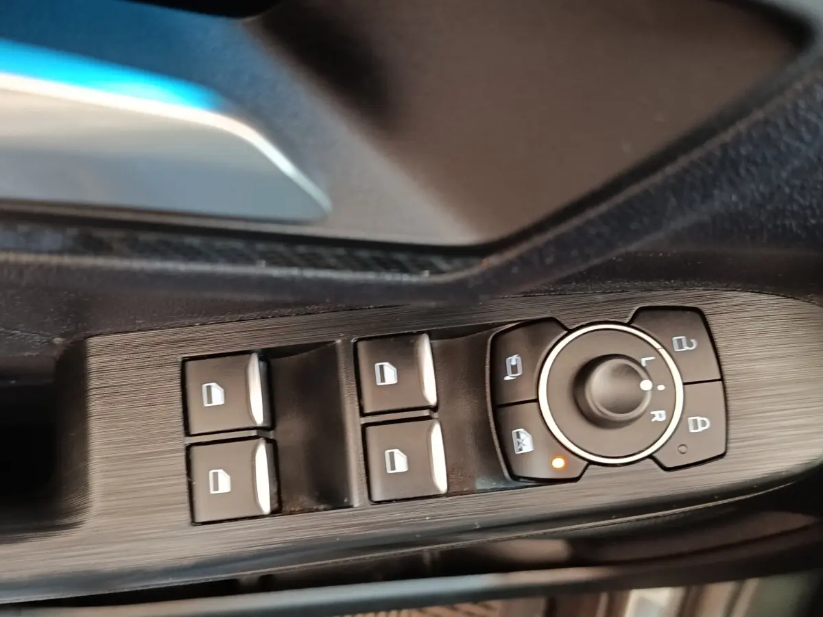 Gros plan sur les commandes de lève-vitres et rétroviseurs côté conducteur du Ford Kuga gris foncé 2023.