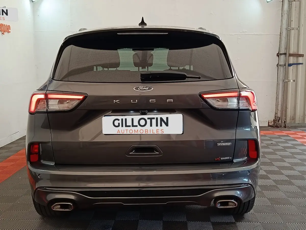 Vue arrière d’un Ford Kuga gris foncé 2023 avec feux LED allumés et double sortie d’échappement rectangulaire.