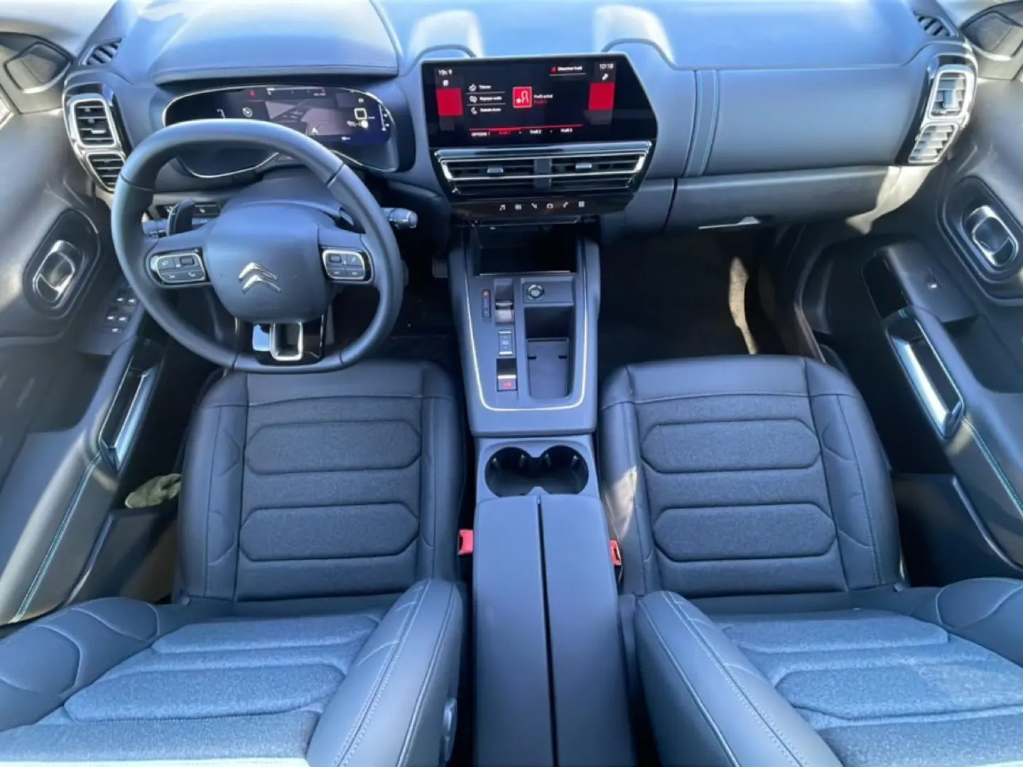 Vue intérieure de face du poste de conduite du Citroën C5 Aircross 2025 avec sièges noirs et écran tactile central.