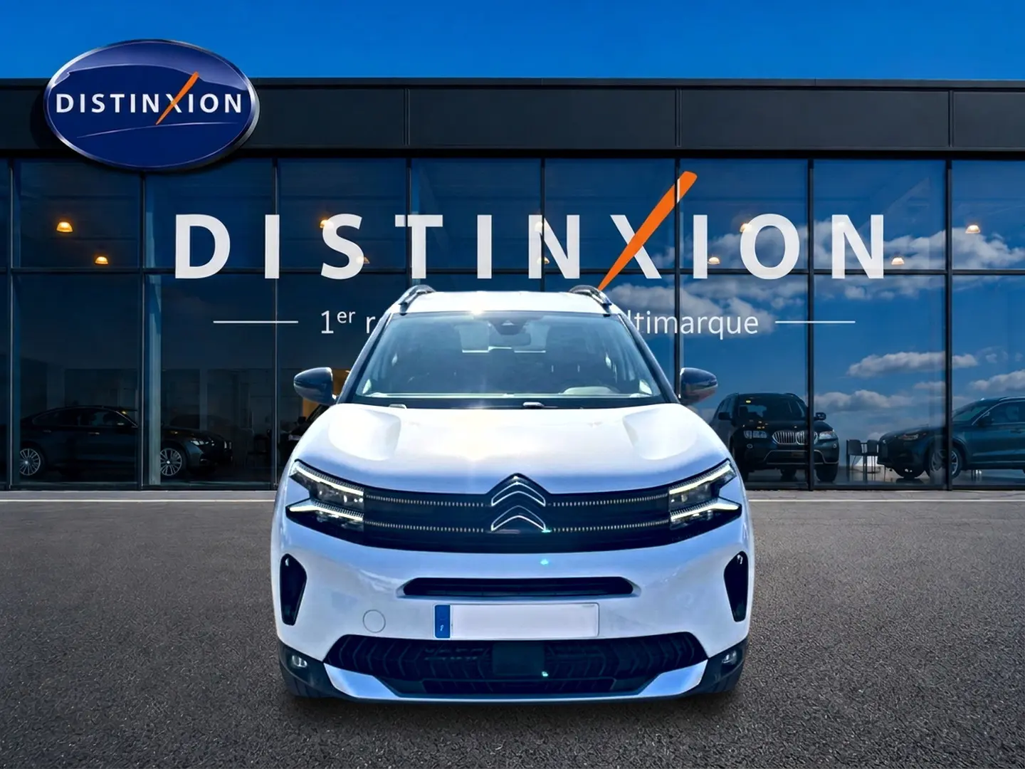 Vue avant d'un Citroën C5 Aircross blanc 2025 avec calandre distinctive et barres de toit visibles devant une vitrine.