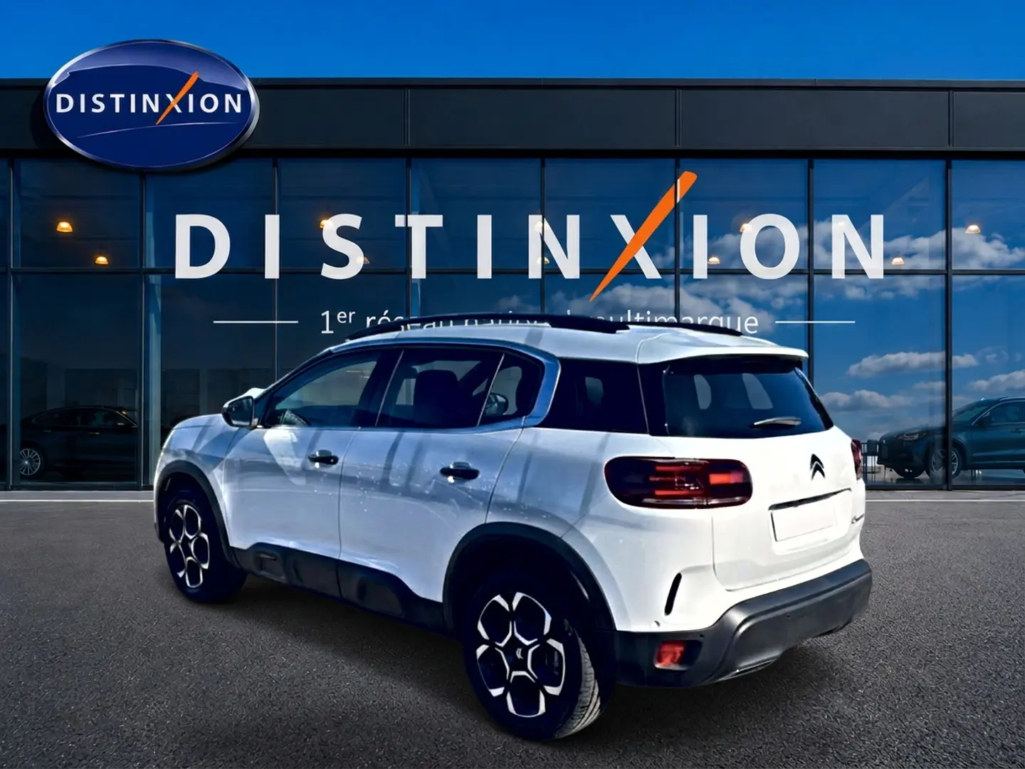 Vue 3/4 arrière droite d'un Citroën C5 Aircross blanc avec jantes alu et barres de toit noires.