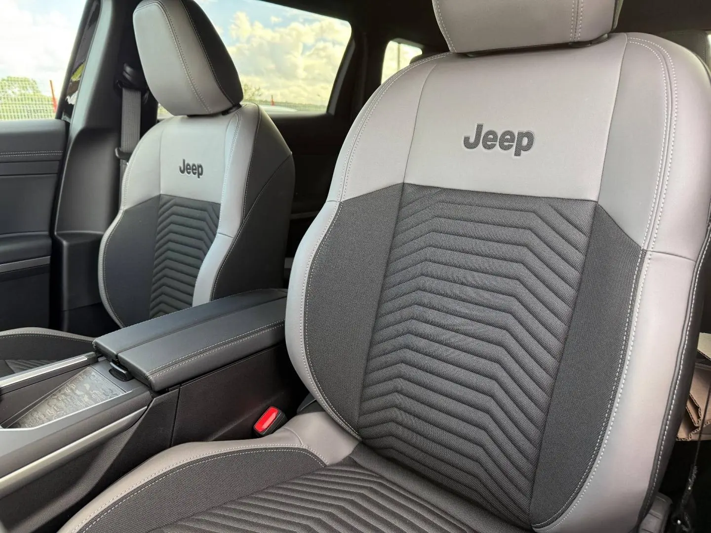 Gros plan sur les sièges avant gris clair et noir avec logo Jeep brodé, accoudoir central et intérieur lumineux.
