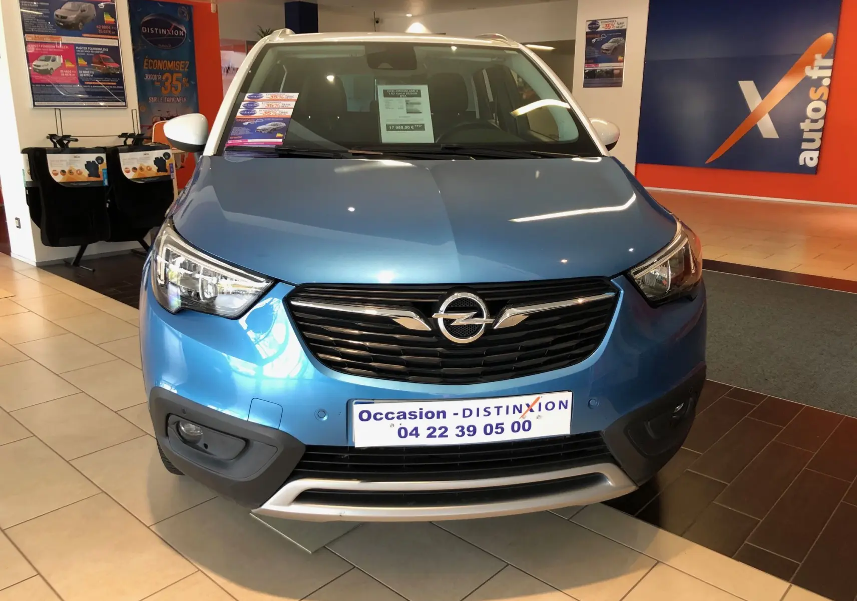 Vue avant d'un Opel Crossland X bleu métallisé exposé en showroom avec calandre noire et détails argentés.
