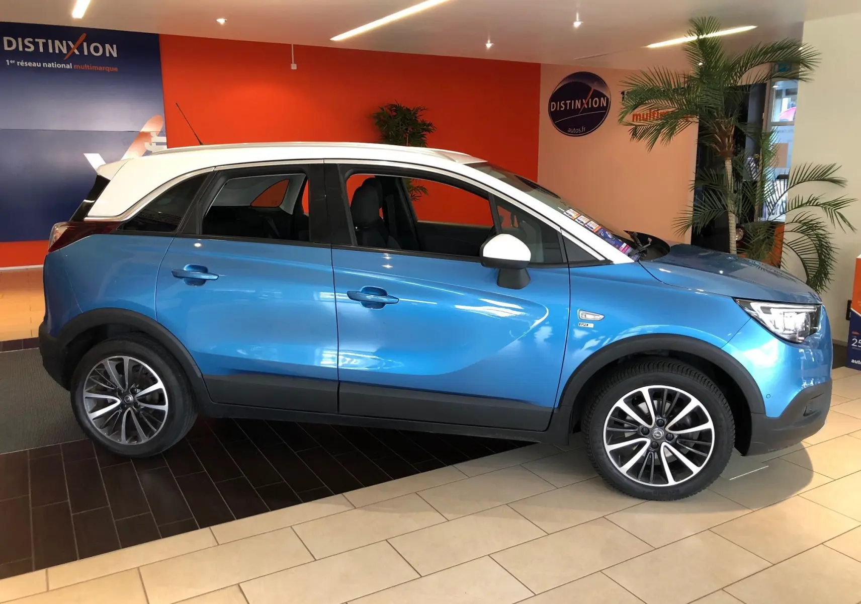 Opel Crossland X bleu intens métal avec toit blanc, vue profil côté gauche en intérieur showroom.