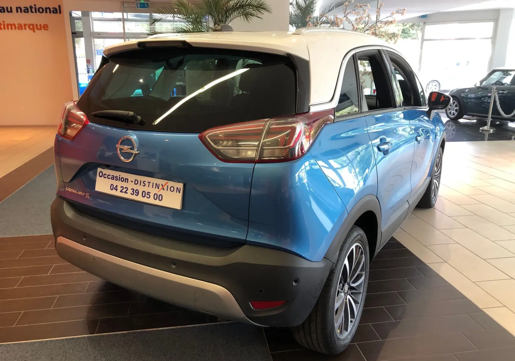 Vue 3/4 arrière droite d'un Opel Crossland X bleu intense métal avec toit blanc en showroom.
