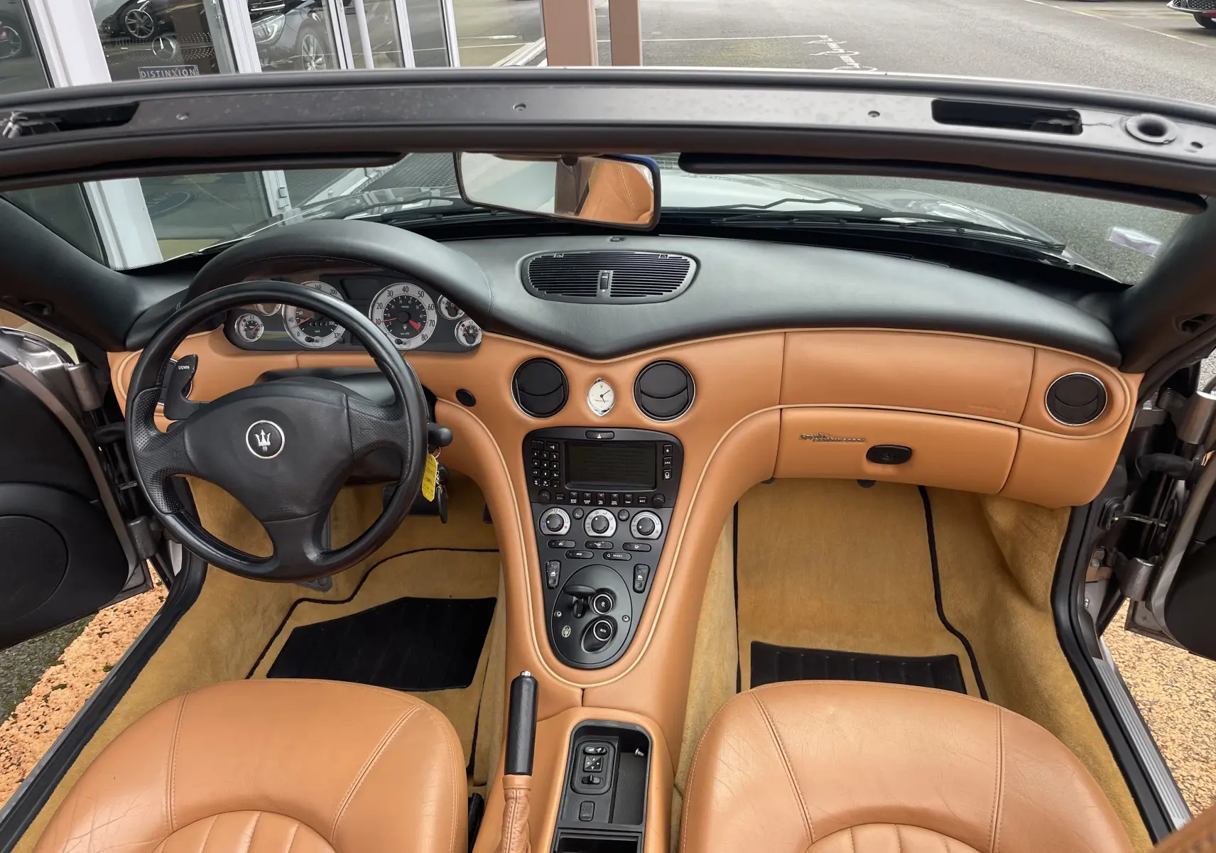 Intérieur cuir beige d'une Maserati Spyder 2002, vue de face sur tableau de bord et volant noir avec logo trident.