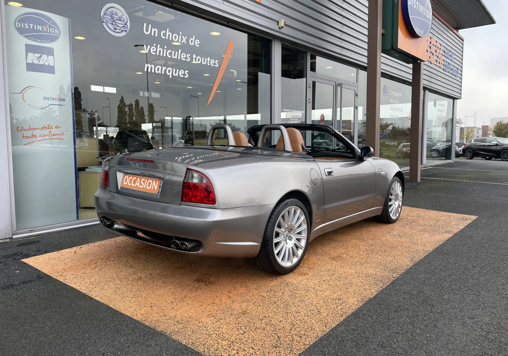 Maserati Spyder gris Nuvolari vue 3/4 arrière droit, capote ouverte et intérieur cuir marron visible.