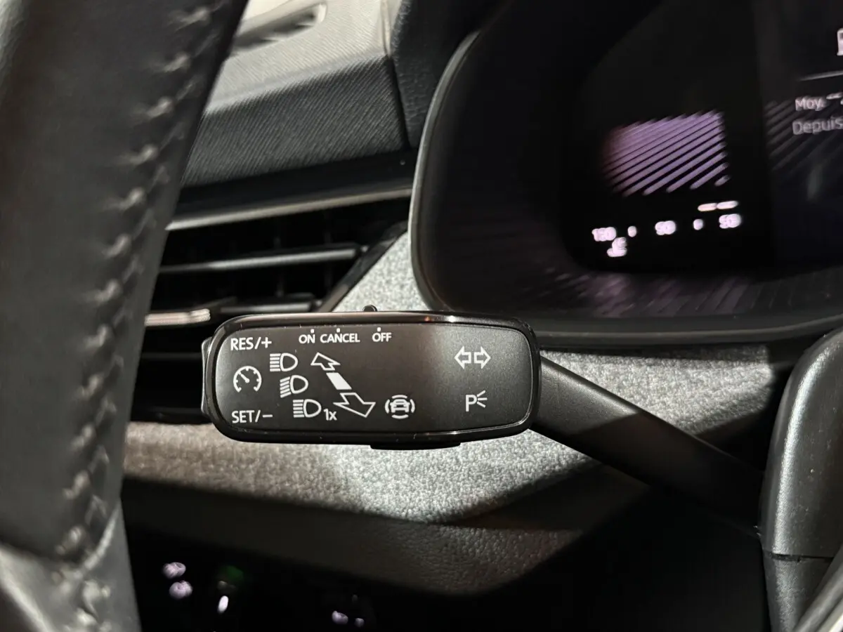 Gros plan sur la commande multifonction côté gauche du volant du Skoda Kamiq rouge 2024, avec affichage digital en arrière-plan.