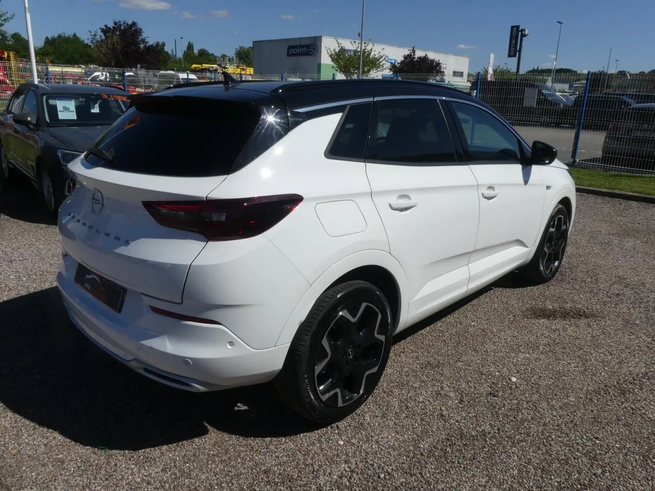 Vue 3/4 arrière droite d'un Opel Grandland blanc métallisé avec toit noir et jantes alliage noires.