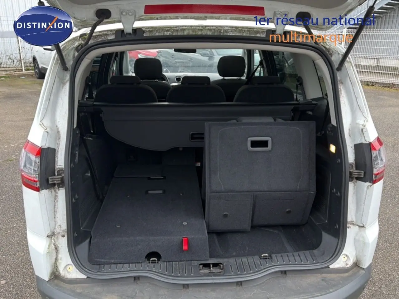 Vue arrière du coffre ouvert du Ford S-MAX blanc, montrant les sièges arrière partiellement rabattus et l'espace de chargement.