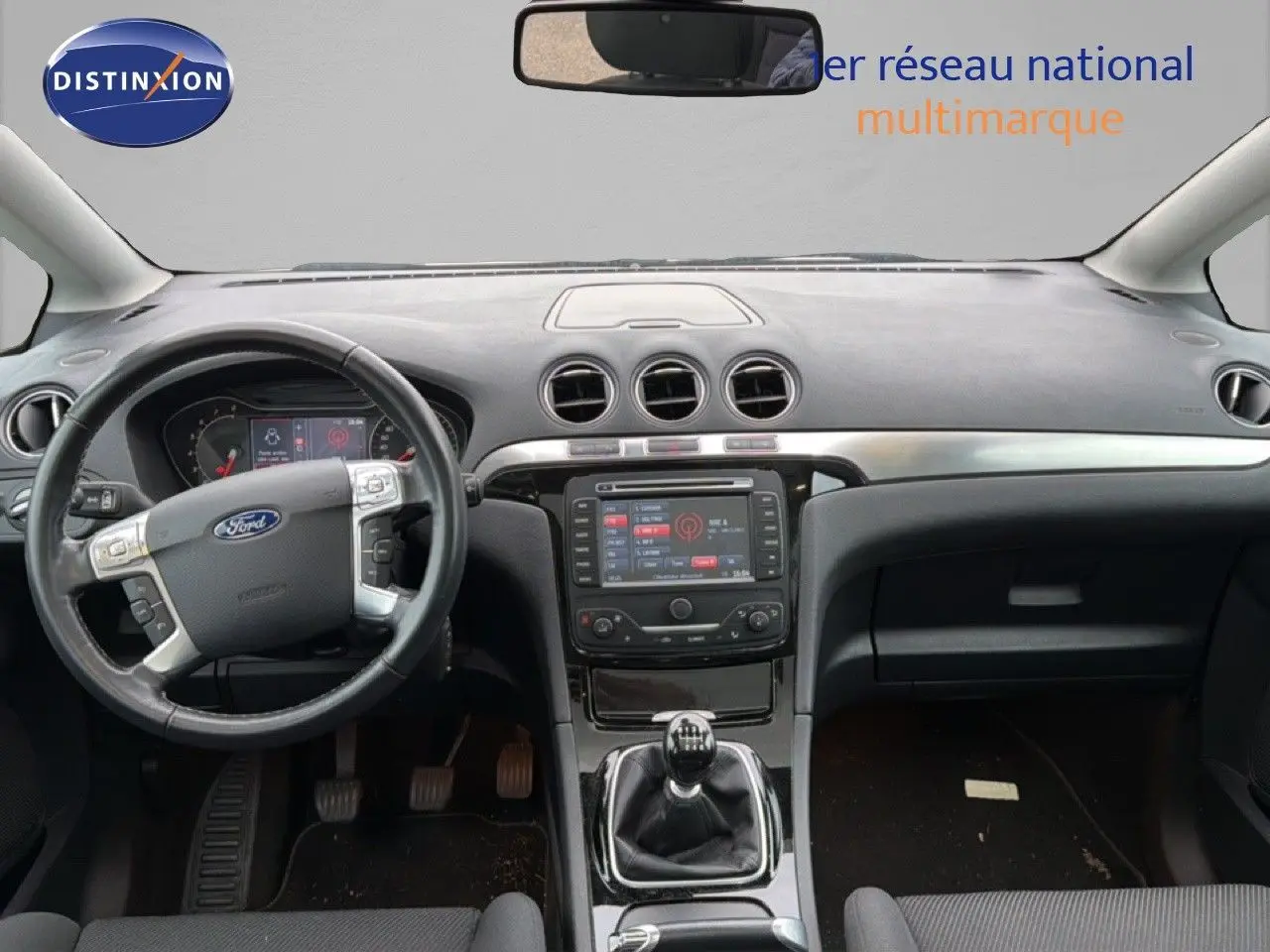 Vue intérieure frontale du tableau de bord et volant noir d’une Ford S-MAX blanche de 2013 avec boîte manuelle.