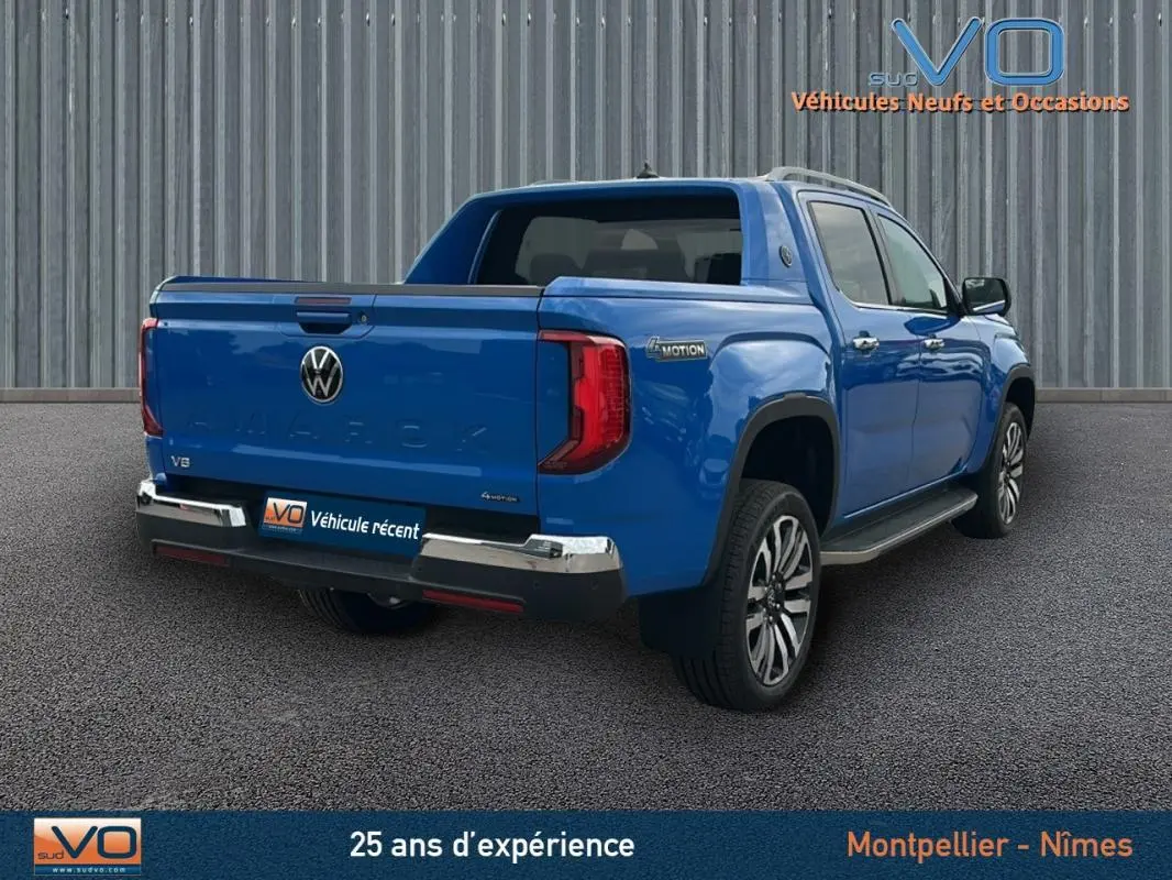 Vue 3/4 arrière droite d'un Volkswagen Amarok bleu avec jantes alliage 21 pouces et marchepieds visibles.