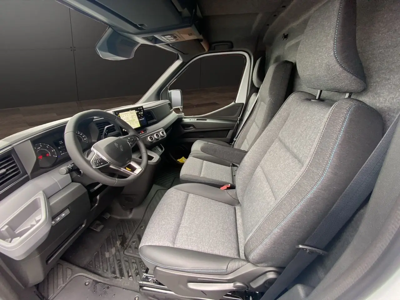 Vue intérieure côté conducteur du Renault Master blanc 2025, sièges tissu gris avec surpiqûres bleues et tableau de bord moderne.