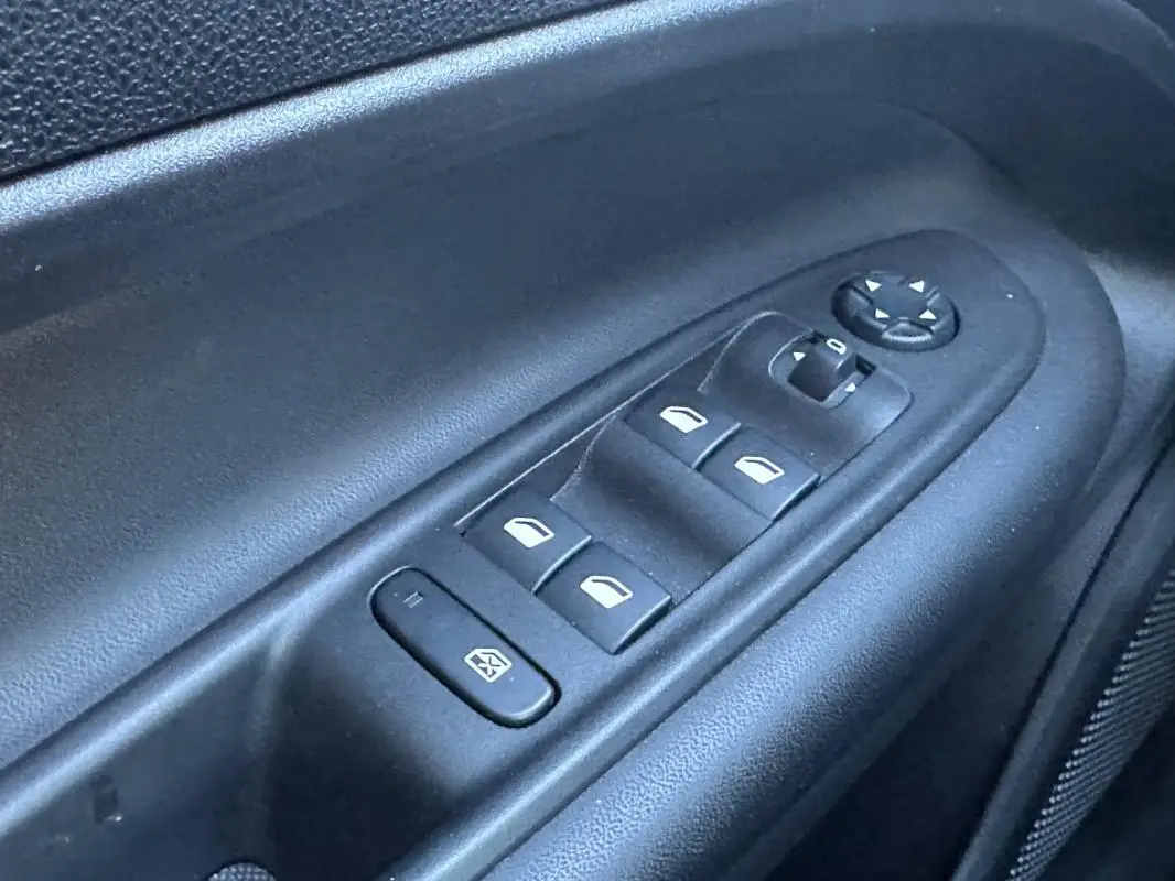Gros plan sur les commandes électriques des vitres et des rétroviseurs côté conducteur d’un Jeep Avenger gris.