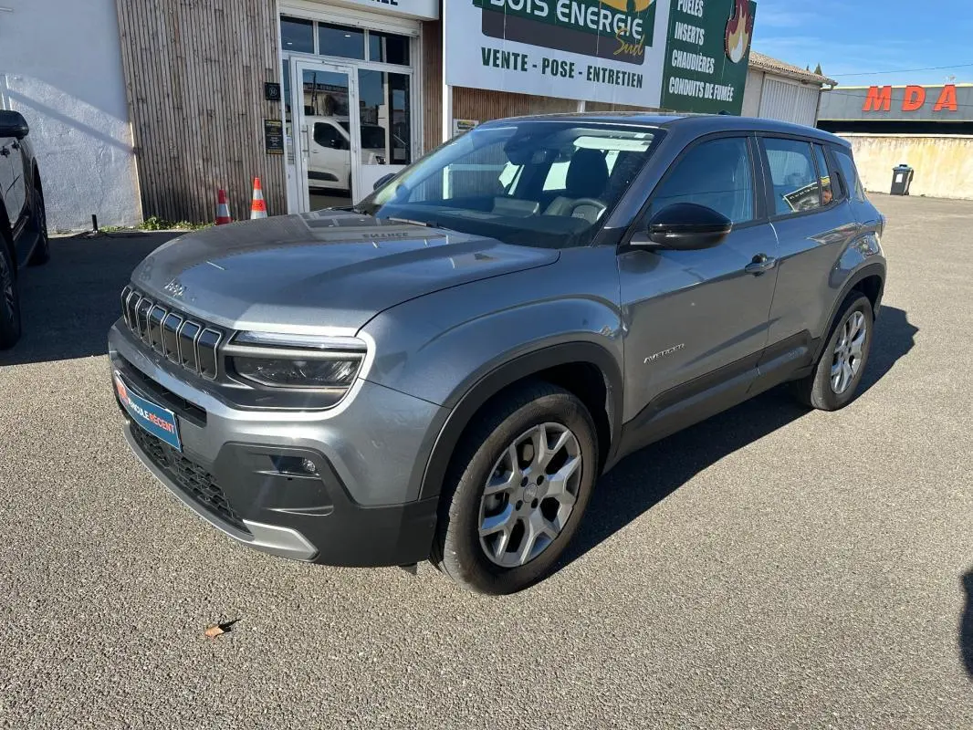 Jeep Avenger gris en 3/4 avant droit, avec jantes alliage 17 pouces et calandre distinctive sous un ciel bleu.