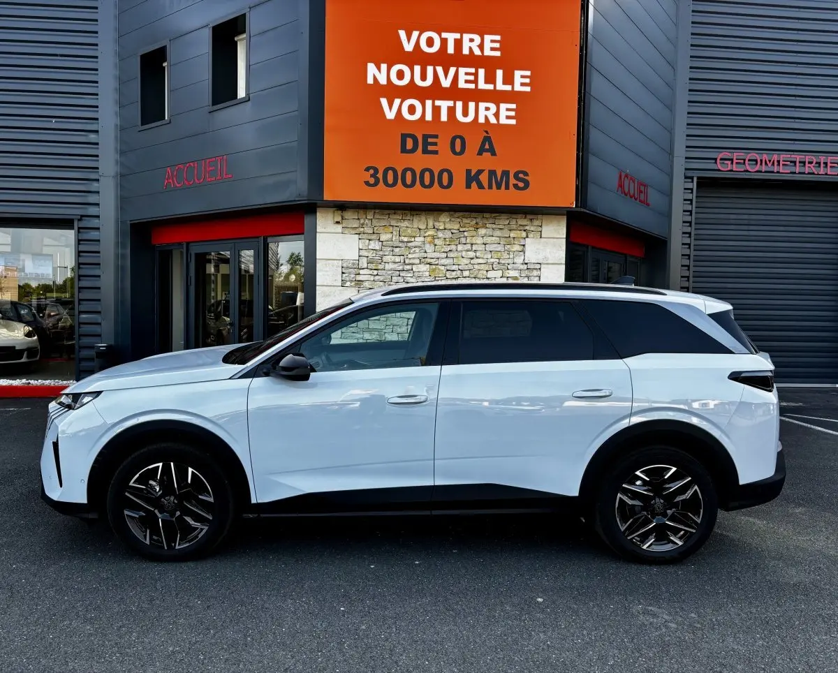 Profil côté gauche du Peugeot 5008 blanc hybride 2025, avec jantes noires et toit contrasté noir.