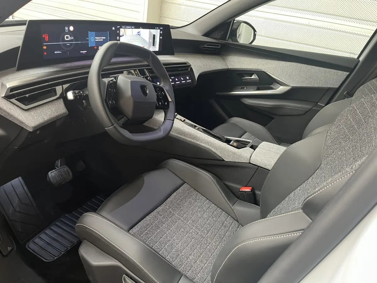 Vue intérieure côté conducteur du Peugeot 5008 Hybrid 2025, volant cuir multifonctions et tableau de bord digital large.