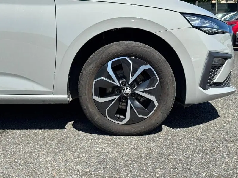 Gros plan sur la roue avant droite d'une Skoda Scala blanche avec jante alu noire et argentée au design géométrique.