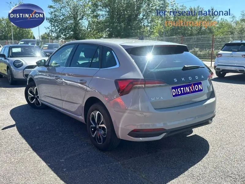 Vue 3/4 arrière droite d'une Skoda Scala bleue 2025 avec jantes alu et feux arrière LED sur parking.