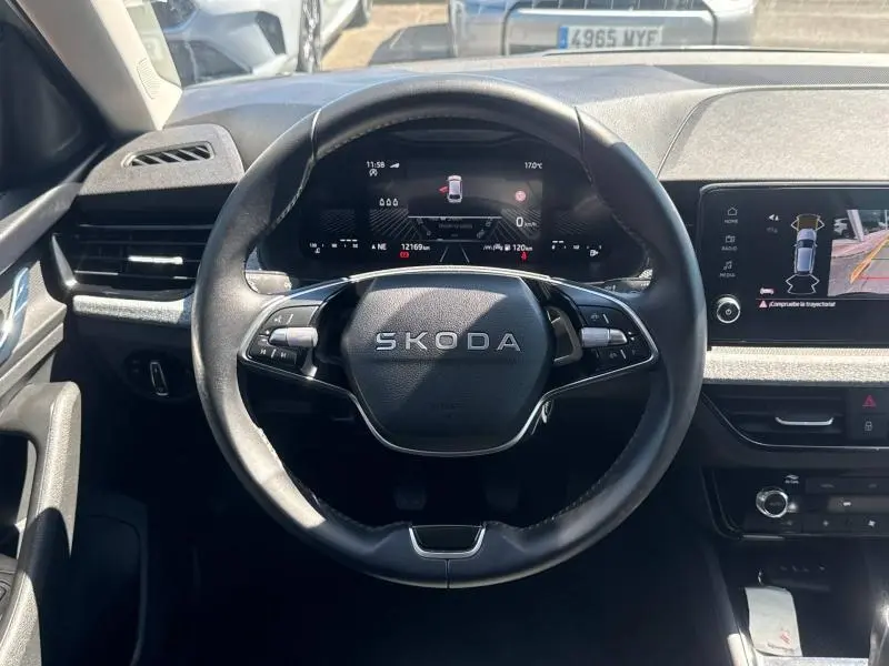 Vue intérieure centrée sur le volant cuir SKODA avec tableau de bord numérique et écran tactile affichant la caméra de recul.