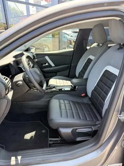Vue intérieure côté conducteur de la Citroën C4 gris foncé 2025, sièges bi-ton cuir noir et gris avec console centrale.