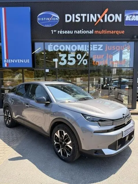 Vue 3/4 avant gauche d'une Citroën C4 gris foncé 2025 stationnée devant une vitrine avec enseigne Distinxion.
