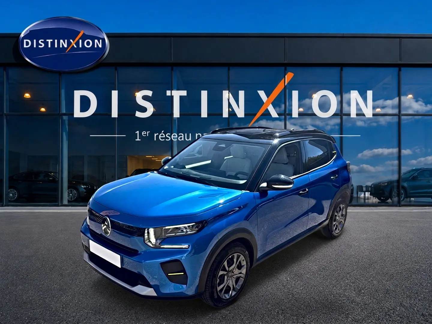 Vue 3/4 avant droite d'une Citroën C3 bleu 2025 avec toit noir et jantes alu devant un bâtiment Distinxion.