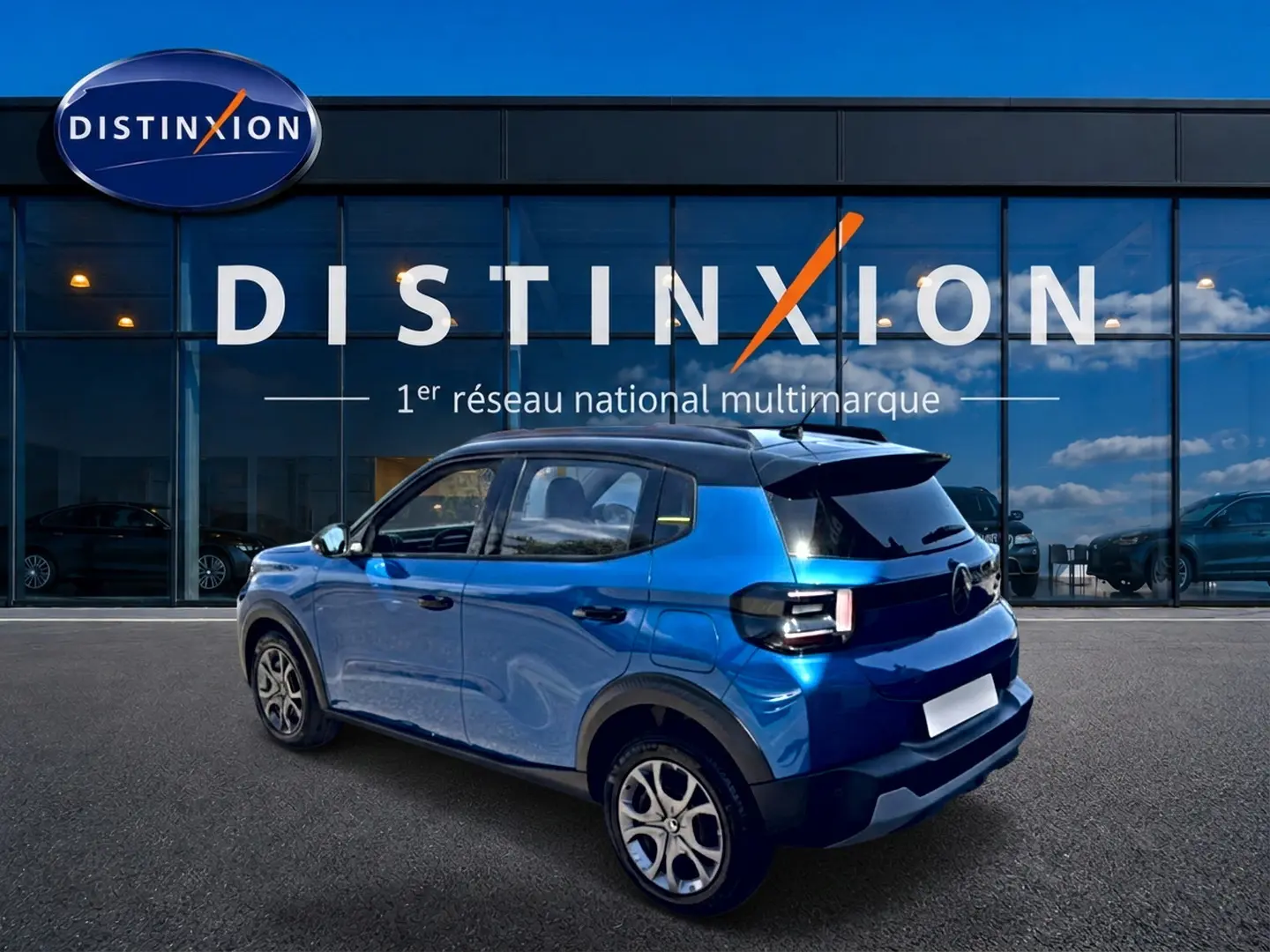 Vue 3/4 arrière droite d'une Citroën C3 2025 bleu avec toit noir et jantes alliage devant une vitrine Distinxion.