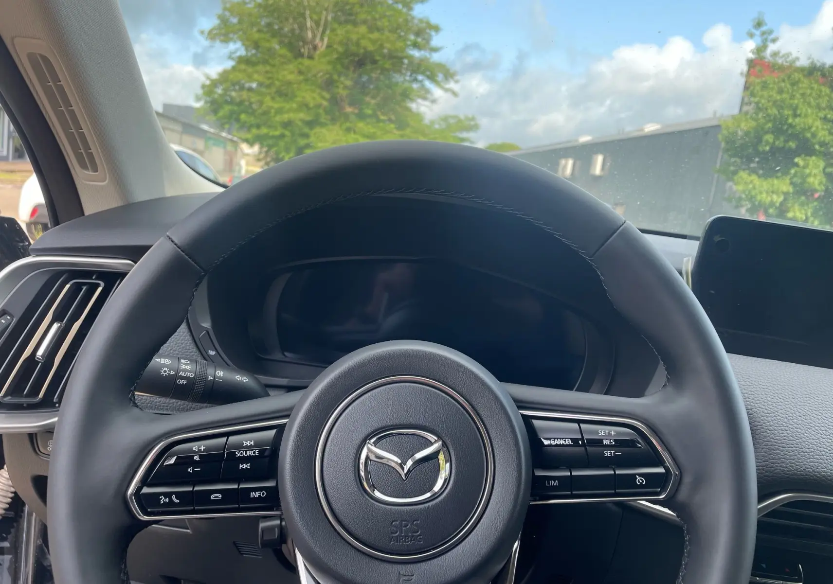 Vue rapprochée du volant en cuir noir du Mazda CX-60 2024, avec commandes intégrées et tableau de bord numérique éteint.