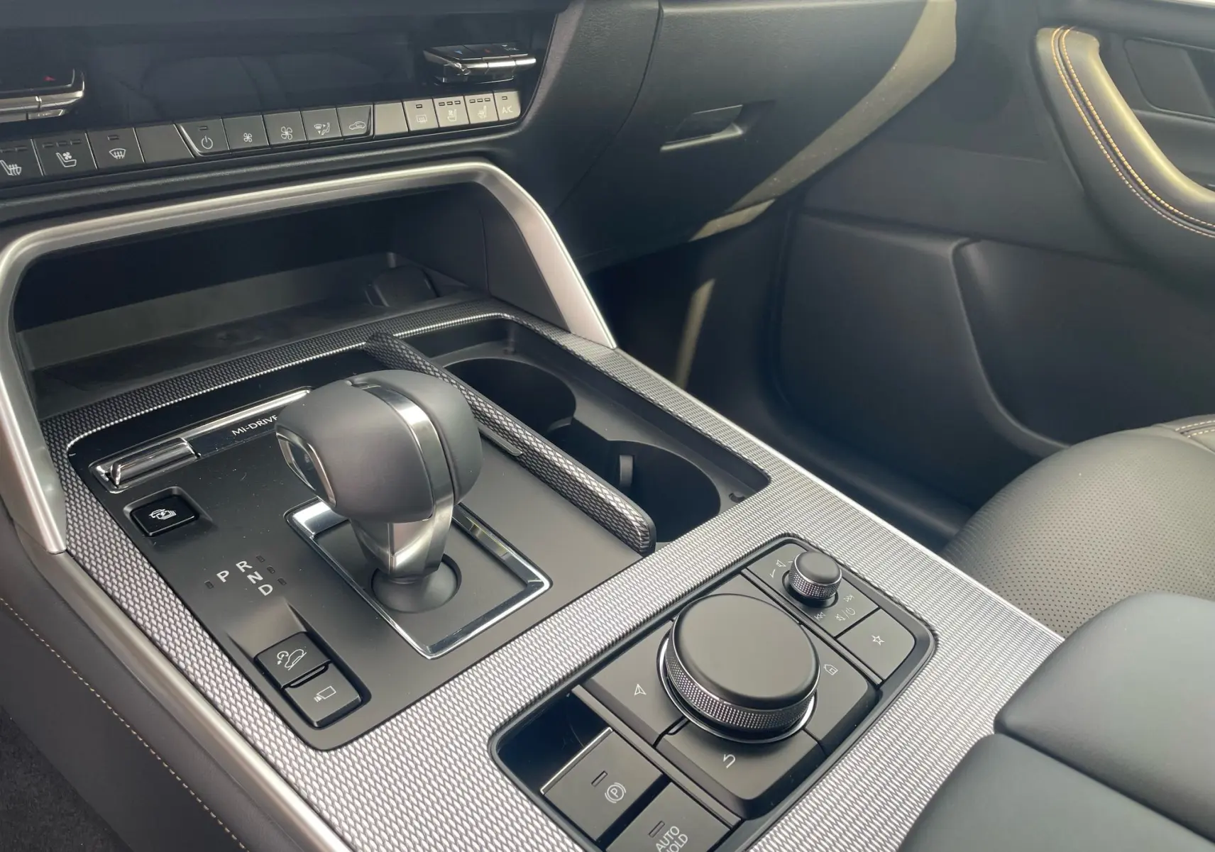 Gros plan sur la console centrale du Mazda CX-60 2024, avec levier de vitesses et commandes sur finition noire et surpiqûres beige.